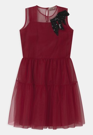 Ærmeløs bordeaux tulle kjole med lagdelt nederdel og gennemsigtig udskæring, der har en sort palietbue detalje på venstre skulder.