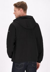 Zwarte waterdichte jas met een capuchon, elastische manchetten en een relaxte pasvorm. Voorzien van een achterventilatie en branding op de linker mouw.