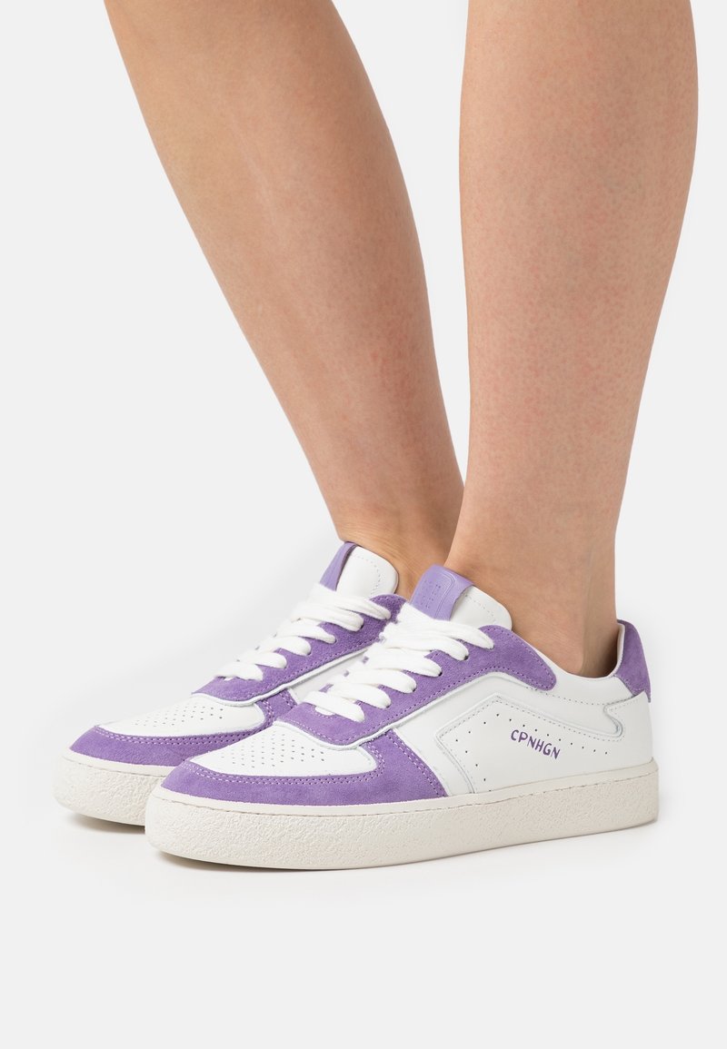 Sneaker bianche con dettagli in suede viola, punta traforata e suola in gomma testurizzata. Presentano lacci piatti e logo sul lato.
