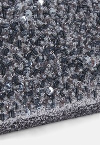 Gros plan de sequins noirs et argentés densément assemblés ainsi que de petites perles sur un tissu texturé.
