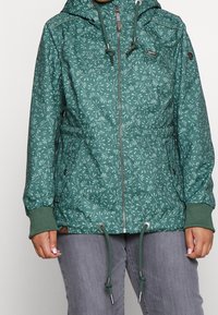 Teal hooded jacket with white floral pattern, front zipper, drawstrings at waist and hood, worn with gray pants.