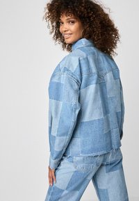 Denim jakk, mis on kaunistatud erinevat tooni sinise lapitehnikaga. Mugav lõige, viimistletud kulunud äärega ja nööbitud varrukaotstega.
