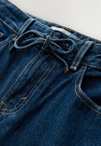 Pantalones cortos de mezclilla de color azul oscuro, con una cintura con cordón ajustable, bolsillos delanteros y costuras con pespuntes amarillos en contraste.