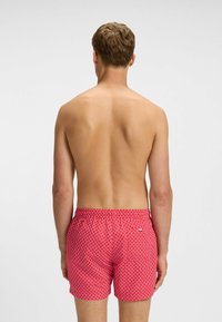 Rode zwembroek met een geometrisch wit patroon, voorzien van een elastische tailleband en een klein logo-label op de achterkant.