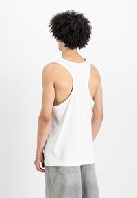 Bela majica brez rokavov s krožnim izrezom. Ima krojen hrbtni del in diskretne šive. Narejena iz mehkega materiala.