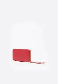 Cartera de cuero roja con acabado texturizado, cierre de cremallera y correa para la muñeca. Forma rectangular compacta, hardware mínimo y bordes lisos.