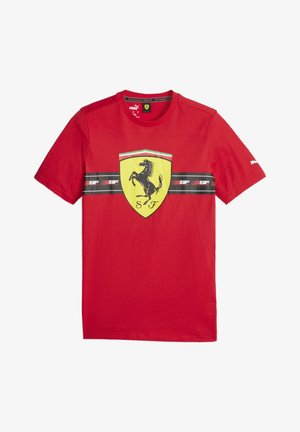 Czerwona koszulka Puma z dużym żółtym logo tarczy Ferrari i czarnym poziomym paskiem z tekstem "SF" na klatce piersiowej.