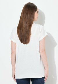 Camiseta blanca de algodón con mangas cortas, corte relajado y cuello redondo. Textura suave y diseño liso, combinada con jeans azules.