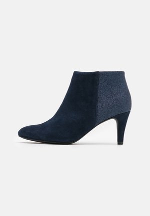 Bottine bleu marine à bout pointu et talon fin de hauteur moyenne, combinant des panneaux en daim et en tissu brillant.