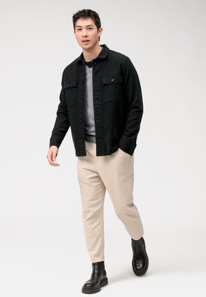 Schwarze Button-Down-Jacke, grauer Rundhals-Pullover, gerippte beige Hose und schwarze Stiefeletten. Lässiges Outfit mit kontrastierenden Texturen und Farbtönen.