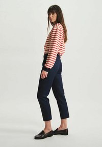 Chemise à manches longues rayée avec des rayures horizontales rouges et blanches, associée à un pantalon cropped bleu marine et des mocassins noirs. Tissu doux et décontracté.