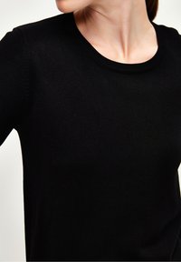 Černý pletený svetr s kulatým výstřihem a přiléhavým střihem, vyrobený z měkké látky s hladkou texturou a minimálním zdobením.