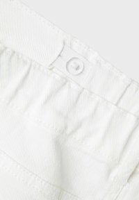 Vit bomullstyg med en texturerad yta, som har en detalj med knapp och elastisk midjeband. Sömmen är snyggt avslutad.