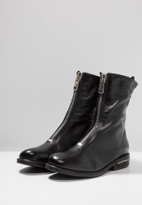 Botas de tobillo de cuero negro con doble cremallera plateada, punteras redondas y un pequeño tacón apilado. Textura suave y diseño minimalista.