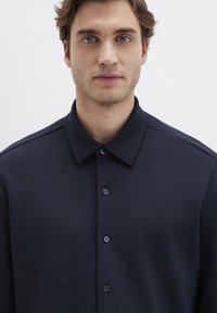 Marineblaues Hemd mit Kragen, aus glattem Stoff gefertigt, mit sechs knopfseilenden Vorderknöpfen und subtilen Schulterdetails.