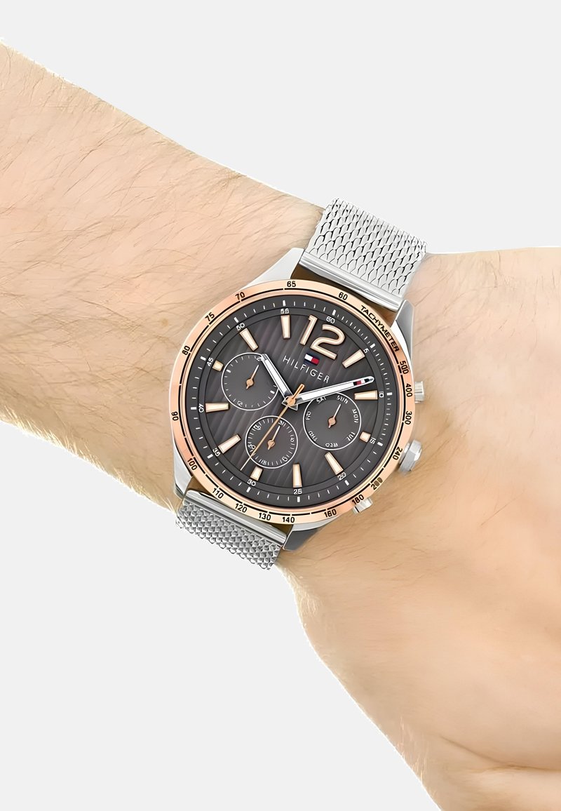 Montre avec un bracelet en maille argentée, un cadran gris foncé, des accents en or rose, de grands chiffres et trois sous-cadrans pour les fonctions de chronométrage.