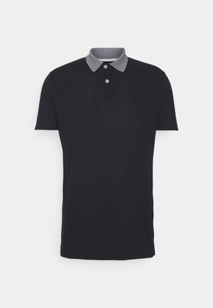 Polo noir à manches courtes avec deux boutons blancs et un col rayé noir et blanc sur un fond uni.