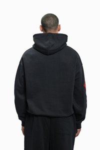 Must suurendatud kapuutsiga pusa, millel on tekstuurse viimistlusega kangas, nööriga kapuuts ja värvilised graafilised trükised varrukaid. 