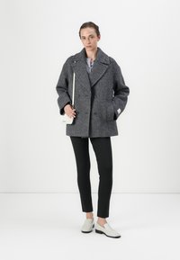 Grå hundetand dobbeltbrystet oversized frakke med brede revers, parret med smalle sorte bukser og hvide slip-on sko.