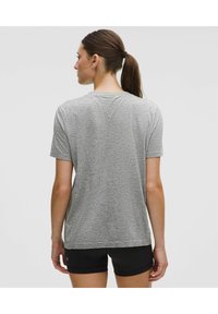 Grå t-shirt med kort ärm och en strukturerad design, rund halsringning och en avslappnad passform, kombinerad med svarta shorts.