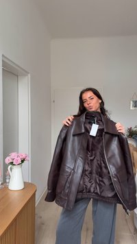 Giacca di pelle marrone con una texture liscia, ampi risvolti e tasche frontali. Presenta una chiusura con cerniera e un'etichetta in tessuto applicata.