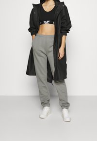 Sort vandtæt lang frakke, tætsiddende sort crop top, grå sweatpants og hvide sneakers. Glatte teksturer og afslappet atletisk stil.