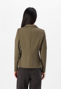 Olijfgroene op maat gemaakte blazer met een gestructureerde silhoutte, geknipte kraag en lange mouwen, met naaddetails aan de achterkant.