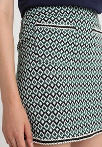 Gonna a pois verde e bianca con un design geometrico, di lunghezza corta, due tasche laterali e un bordo decorativo bianco all'orlo.