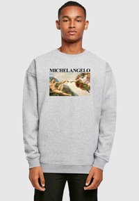 Hanorac gri cu imprimeu pe partea din față inspirat de opera lui Michelangelo, având textul "MICHELANGELO" deasupra imaginii. Mâneci lungi și mansete cu striații.