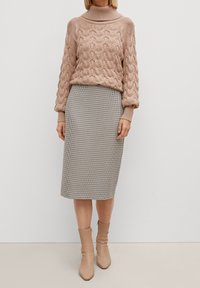 Pull en tricot torsadé de couleur rose pâle avec un col montant, associé à une jupe crayon à motifs pied-de-poule arrivant au genou et des bottines beige.