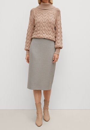 Suéter de punto trenzado en color rosa pálido con un cuello alto, combinado con una falda lápiz de longitud a la rodilla con patrón de pata de gallo y botas de tobillo beige.