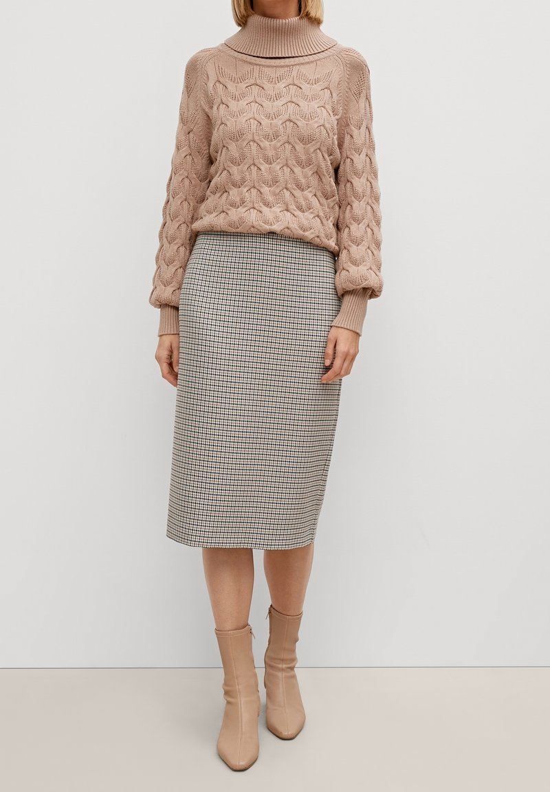 Pull en tricot torsadé de couleur rose pâle avec un col montant, associé à une jupe crayon à motifs pied-de-poule arrivant au genou et des bottines beige.