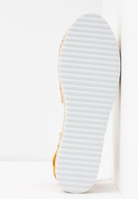 Semelle d'une chaussure avec une semelle extérieure en caoutchouc blanche rainurée faisant face à une surface murale blanche d'angle.