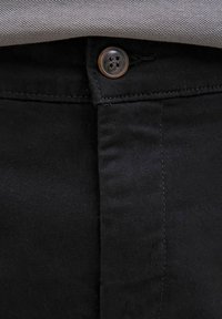 Κοντινή λήψη μαύρου παντελονιού κουμπωμένου στη μέση με γκρι υφασμάτινο πουκάμισο που είναι μπαίνει μέσα πάνω από τη μέση.