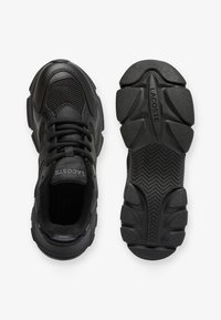 Zapatillas negras con parte superior de malla y sintético, punta redonda y cuello acolchado. La suela presenta un agarre texturizado con el logotipo "LACOSTE".