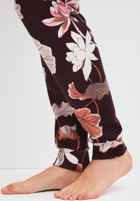 Pantalons à motifs floraux violets ornés de fleurs de lotus blanches et roses, avec des feuilles vertes, fabriqués dans un matériau doux et extensible.