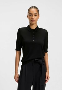 Polo shirt nero a maniche corte realizzato in un materiale liscio, con colletto classico e chiusura a sei bottoni. Completato da una vestibilità rilassata.