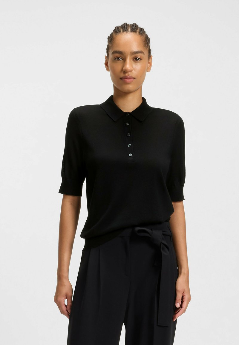 Polo shirt nero a maniche corte realizzato in un materiale liscio, con colletto classico e chiusura a sei bottoni. Completato da una vestibilità rilassata.