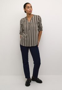 Camisa de botones a rayas verdes y blancas con mangas enrolladas, combinada con jeans azul oscuro y mocasines negros, sobre un modelo contra un fondo neutro.
