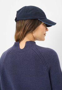 Marineblauwe pet met een gebogen rand, voorzien van een lichtblauwe accentvorming aan de rand. Woltrui met een gestructureerd oppervlak en een splitneklijn detail.