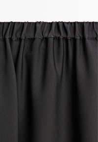 Tessuto nero con una texture liscia e un bordo superiore arricciato. Il materiale appare leggero e scende verso il basso in pieghe sottili.