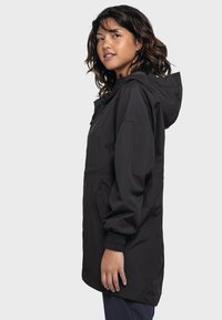 Schwarze Regenjacke mit Kapuze, elastischen Bündchen und tailliertem Schnitt. Das Material scheint wasserabweisend zu sein und hat eine glatte Textur.