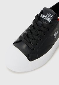 Zwarte leren sneaker met een witte rubberen neuskap, voorzien van een zwart vetersysteem, een gestructureerd oppervlak en "LOVE MOSCHINO" branding op de tong.