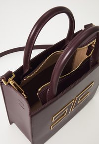 Sac à main en cuir bourgogne avec quincaillerie dorée, deux poignées et une fermeture à glissière supérieure. L'intérieur comprend deux poches zippées et une doublure lisse.