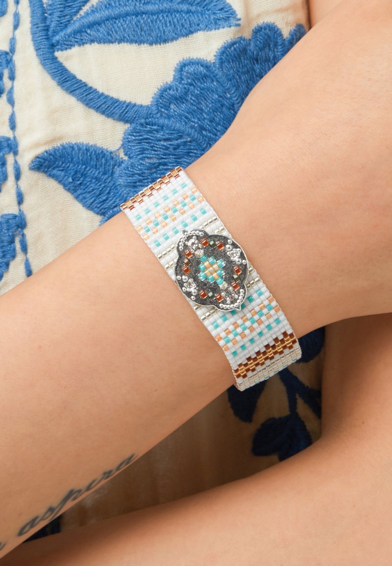 Bracelet tressé en perles turques, corail et blanc avec un accent décoratif central en tone argenté présentant des détails ornés de bijoux.