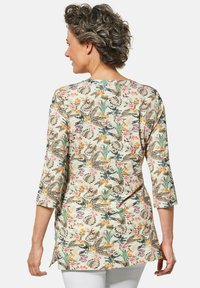Langermige tuniek met een bloemenpatroon in groen, geel en roze, op een lichte achtergrond; gebogen zoom en een ontspannen pasvorm.