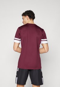 Bordeaux sportshirt met witte streepaccenten op de mouwen, met een ronde hals en een aansluitende pasvorm. Van achteren gezien.