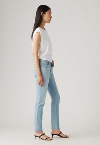 Fehér ujjatlan felső, világoskék farmernadrág, és fekete magassarkú szandál. Slim fit farmernadrág, elhalványult mosással, sima textúrával és minimális részletezéssel.