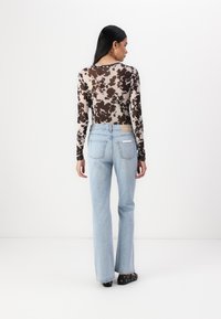 Långärmad, figurnära blus i brunt och krämfärgat koskinnsmönster, tillsammans med ljusblå, utsvängda jeans. Båda har subtila sömmar och detaljer i metall.