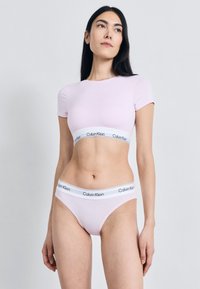Ροζ ελαστικό βαμβακερό crop top με κοντά μανίκια, σε συνδυασμό με ταιριαστό εσώρουχο τύπου thong χαμηλής μέσης. Εμφανές λογότυπο στις ελαστικές ζώνες στη μέση σε αντίθετο λευκό χρώμα.